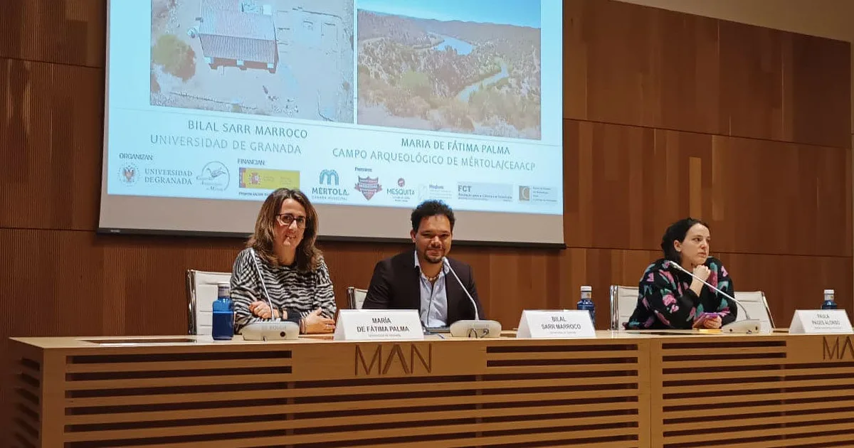 Conferência académica com três palestrantes em auditório.