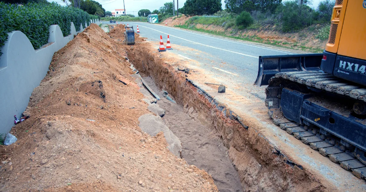 Obras na estrada com escavadora e sinalização.