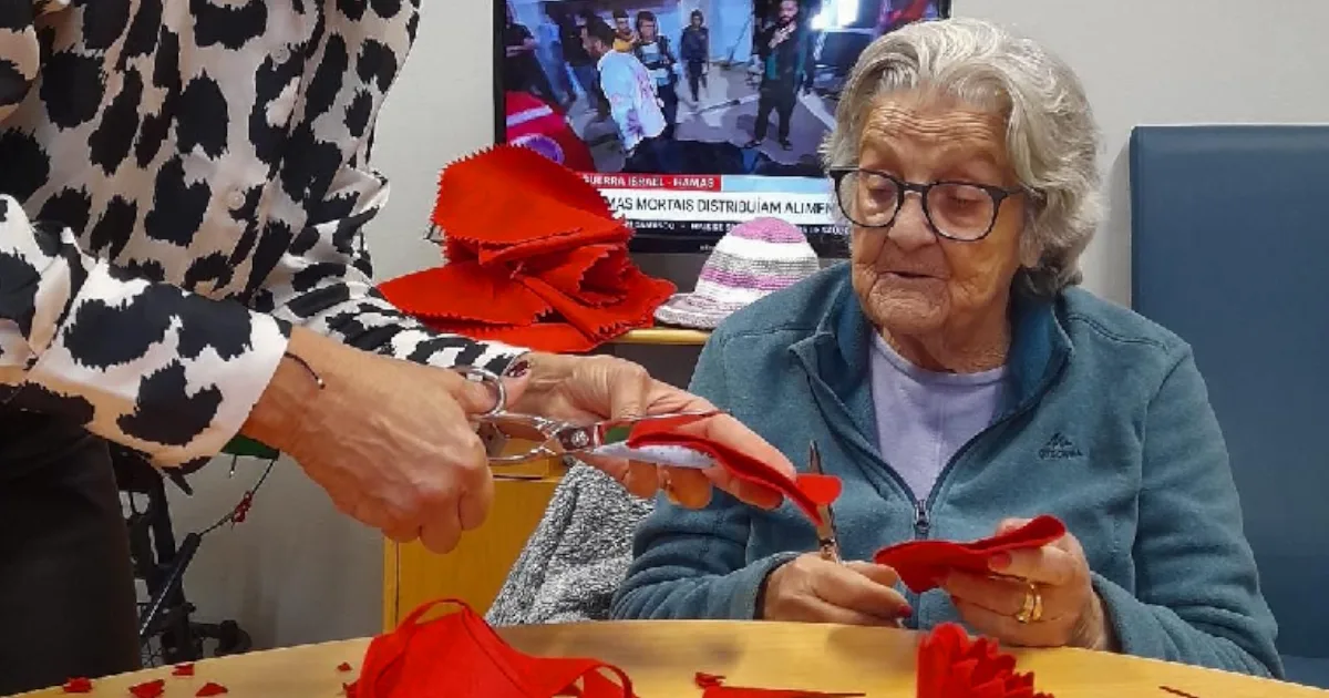 Senhora idosa fazendo artesanato em tecido vermelho.