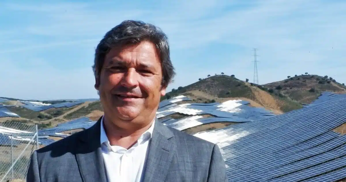 Homem sorrindo com painéis solares ao fundo.